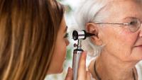 Doctor holding otoscope and examining ear of senior woman
